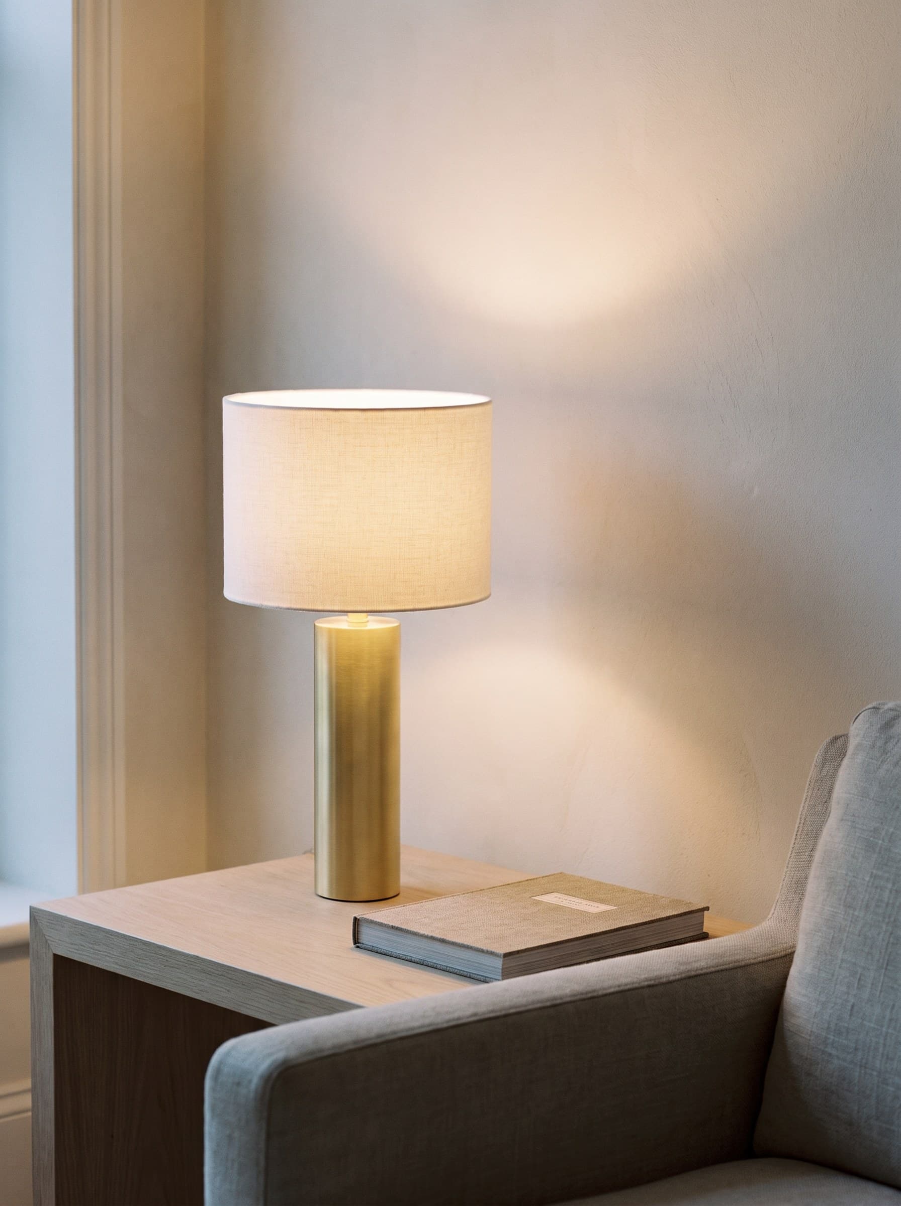 A brass table lamp lit on an oak side table against a warm plaster wall.